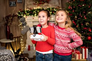 Dos niñas pequeñas iniciándose en la aeronáutica con un dron al lado del arbol de navidad.