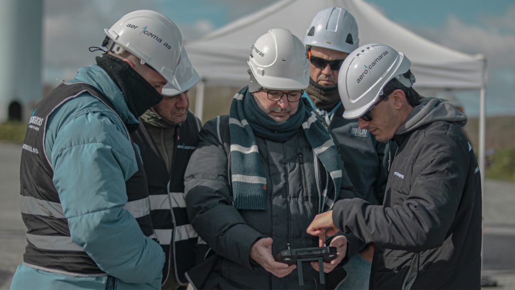 grupo de inspectores técnicos de campos eólicos con cascos blancos realizando su trabajo con drones